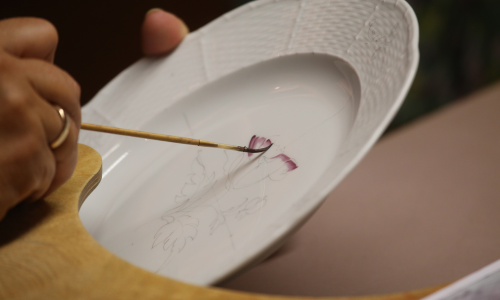 Een persoon schildert een bloem op een wit porseleinen bord